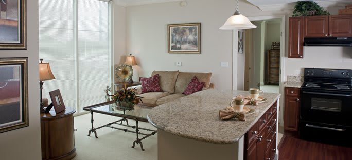 A cozy living room with a beige sofa, glass coffee table, and adjacent kitchen counter.