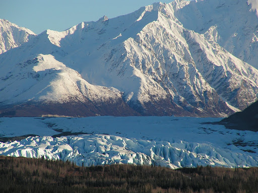 A breathtaking view of a glacier surrounded by majestic snow-capped mountains.