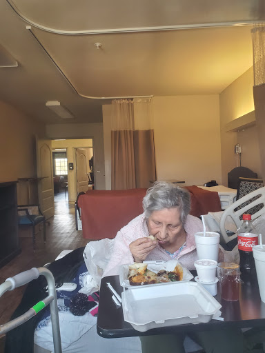 An elderly woman enjoying a meal in a cozy care facility setting.