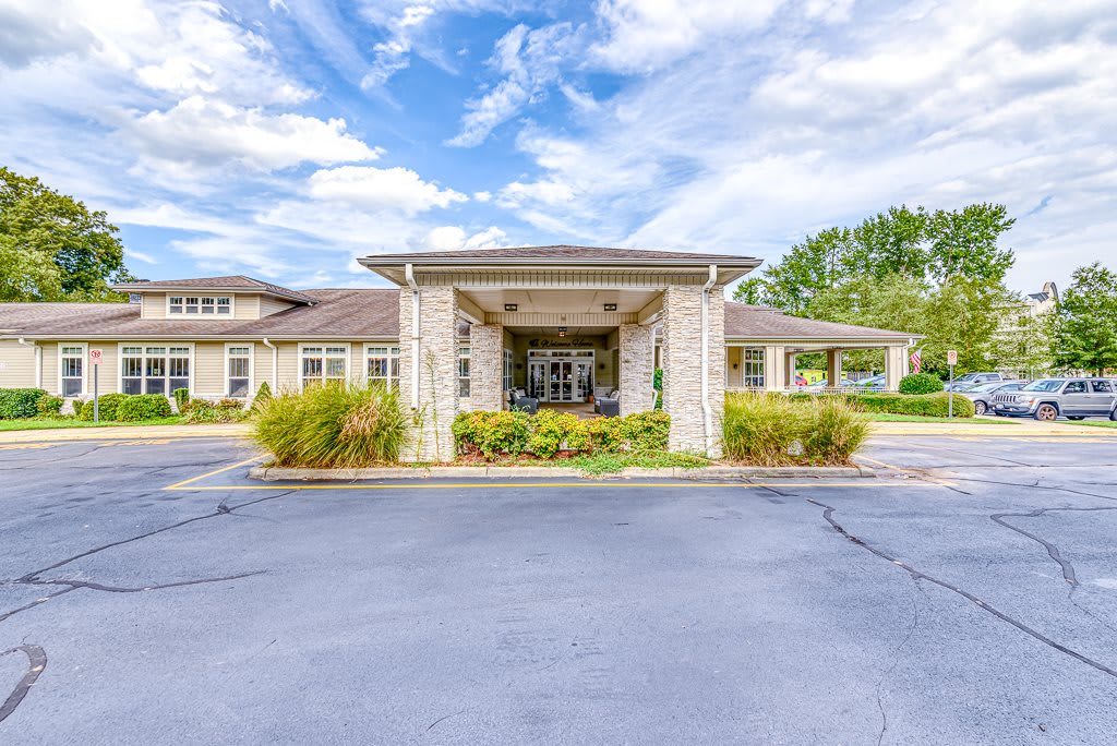 Front entrance of a building with a covered driveway and landscaped surroundings on a clear day.