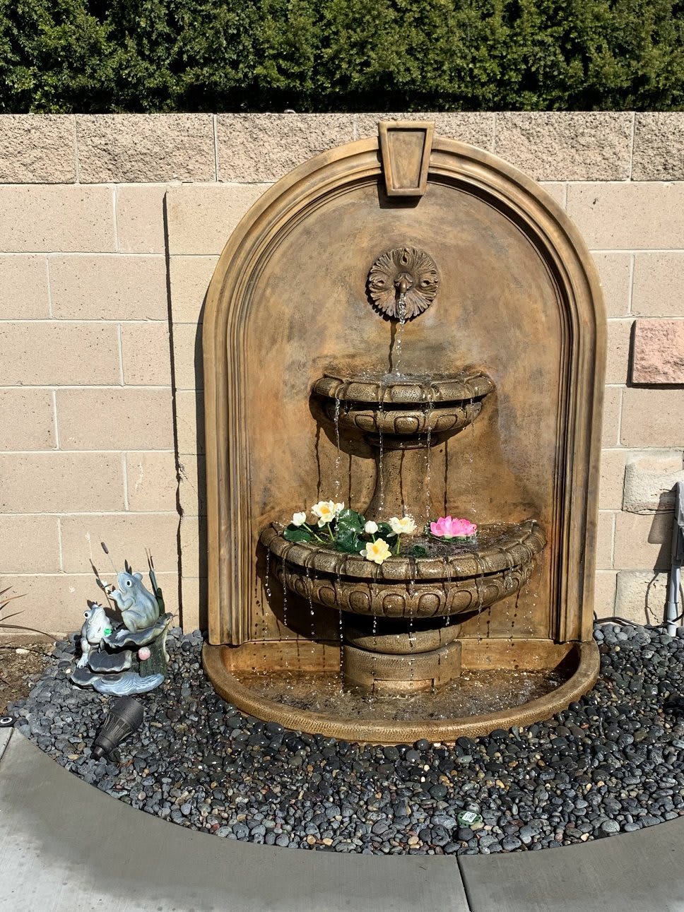 A decorative wall-mounted fountain with flowers floating in the basins.