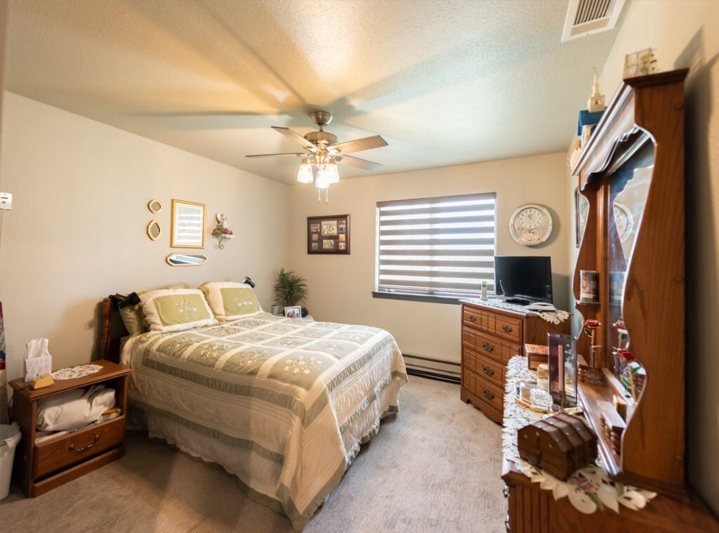 A cozy bedroom interior with neatly arranged furniture and a ceiling fan.