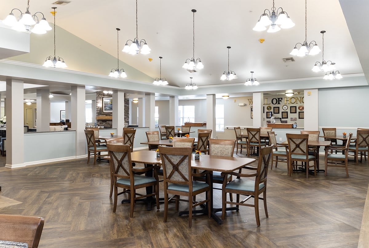 A spacious and modern dining area with wooden floors, round tables, and stylish chairs, illuminated by multiple hanging light fixtures.