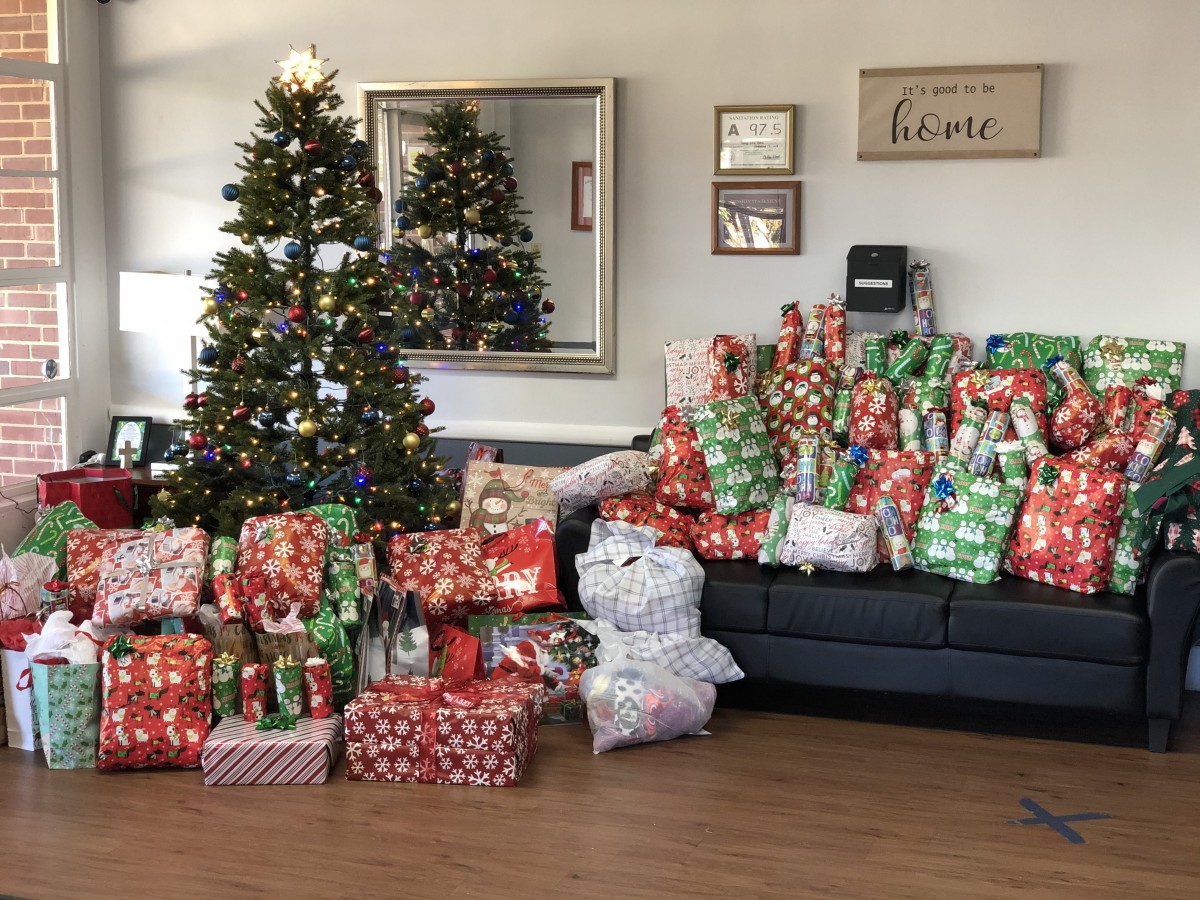 A festive living room with a decorated Christmas tree and a sofa piled high with colorful wrapped presents.