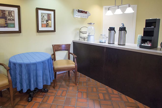 A small beverage area with a coffee station and a table with a chair.