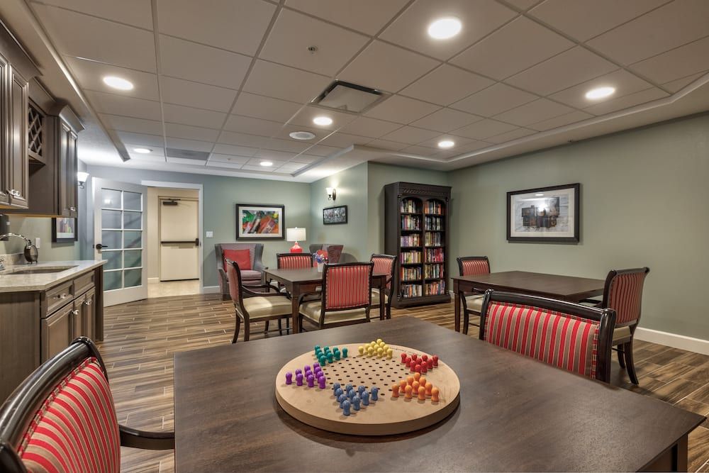 A cozy indoor game room with a Chinese checkers board on the table, surrounded by chairs and bookshelves.