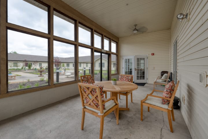 A cozy patio area with a round table and chairs, featuring large windows providing an outdoor view.