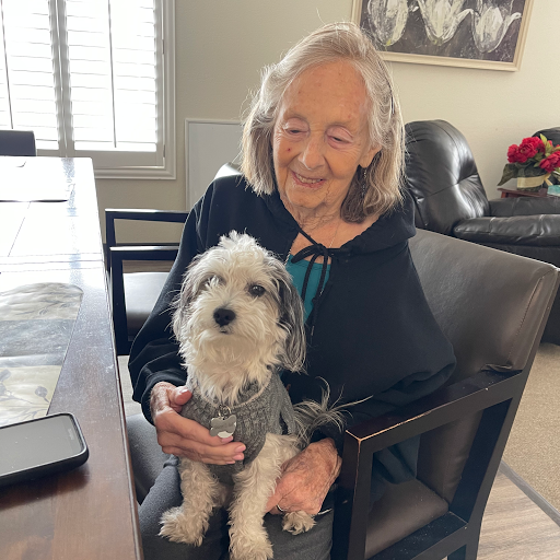 An elderly woman sitting at a table, happily holding her small dog.