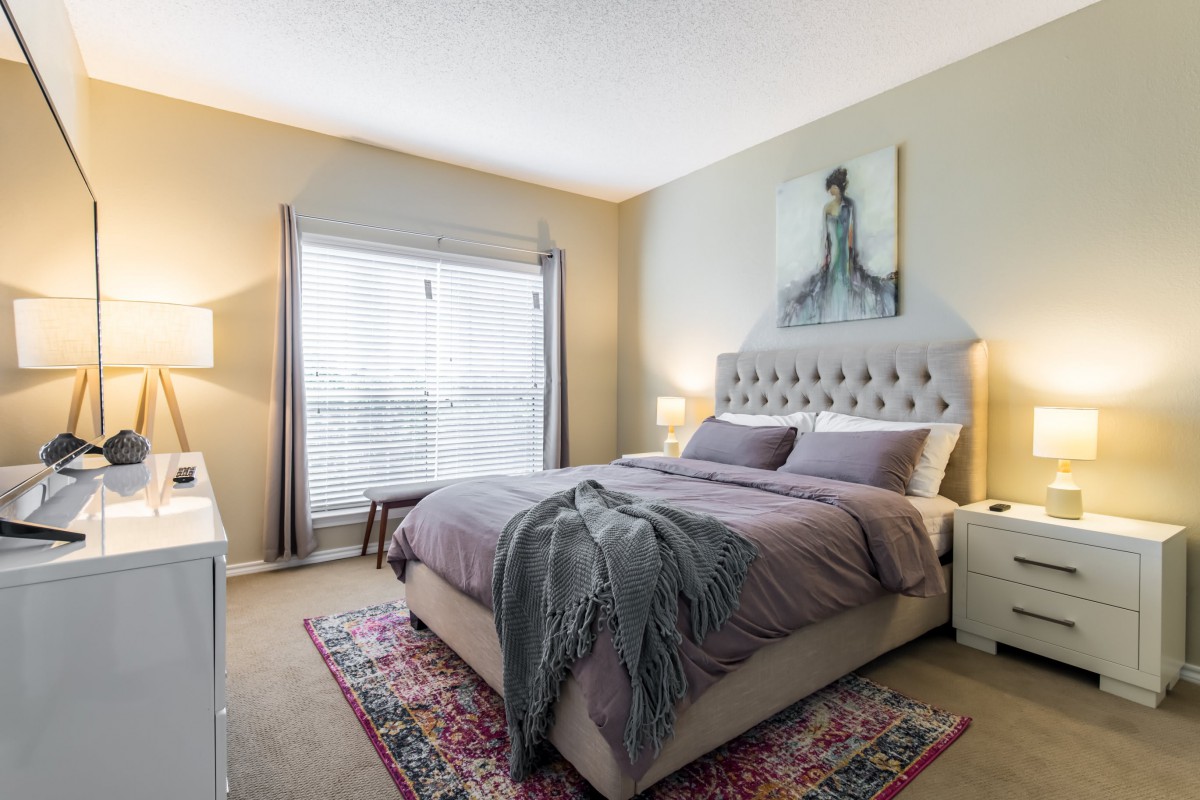 A cozy bedroom with a neatly made bed, featuring a tufted headboard and decorative artwork on the wall.