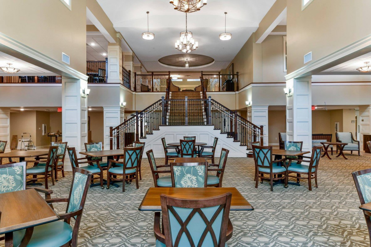 Spacious and elegant lobby area with tables, chairs, chandeliers, and a grand staircase.