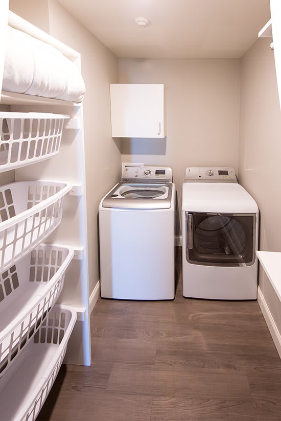 A compact laundry room featuring a washing machine, dryer, and organized storage shelves with baskets.