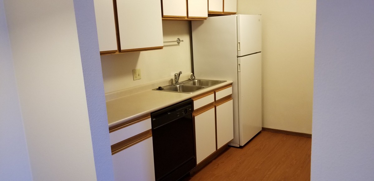 A compact apartment kitchen with white cabinets and standard appliances.