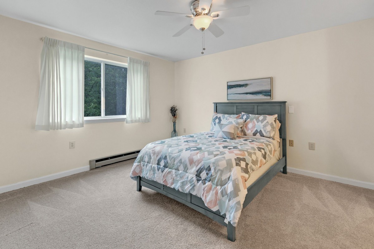 A cozy bedroom with a patterned bedspread, large window, and ceiling fan.