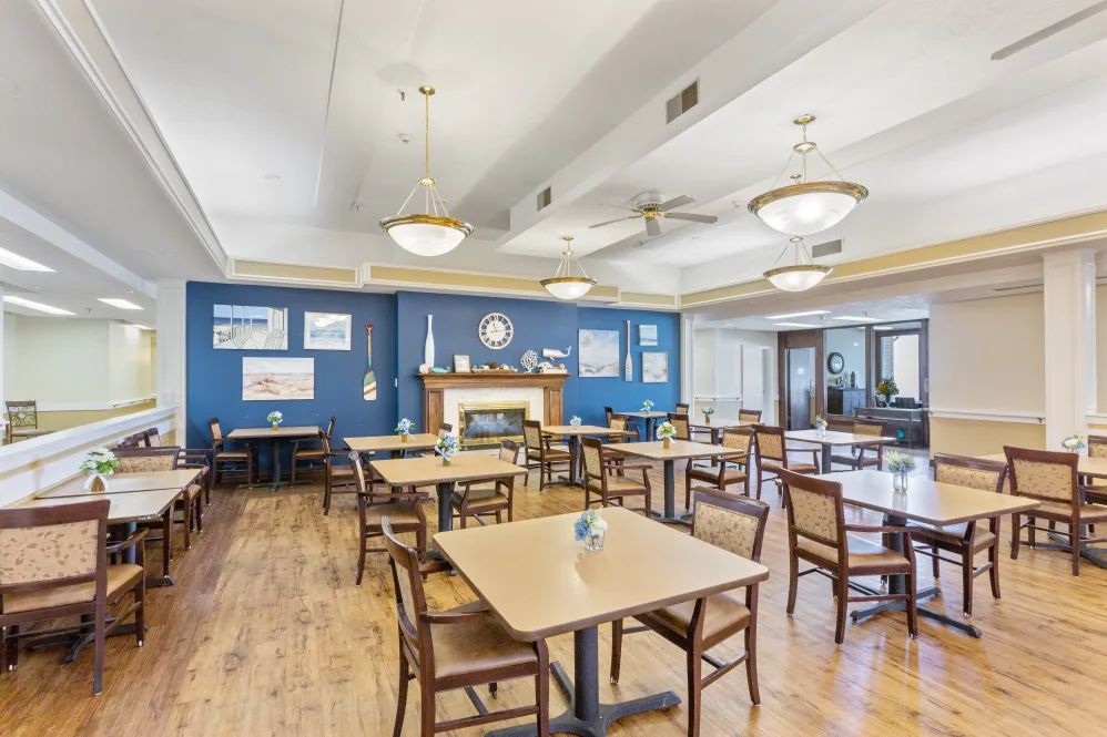 A spacious dining room with wooden floors, tables, and chairs set against a blue accent wall adorned with art.