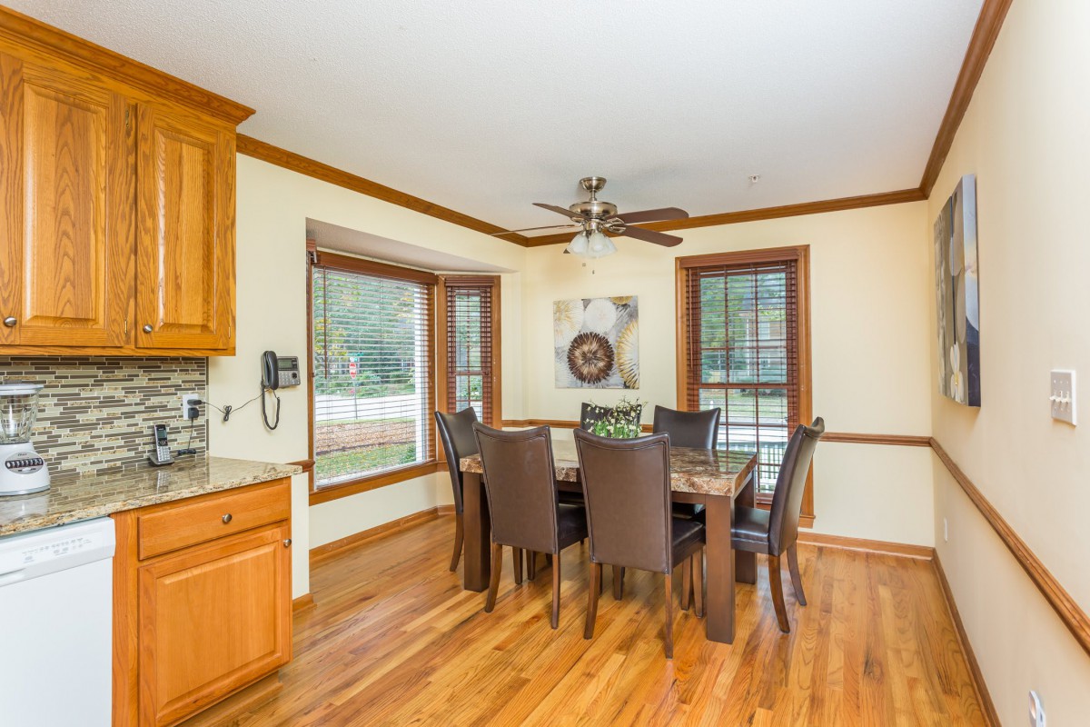 A cozy dining area with a wooden dining table and chairs, featuring hardwood flooring and ample natural light from multiple windows.