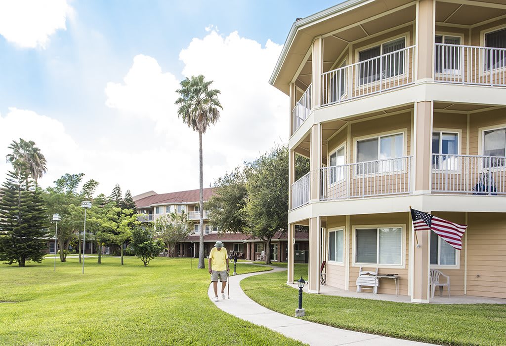 A sunny day view of an apartment complex with a well-maintained lawn and a palm tree.