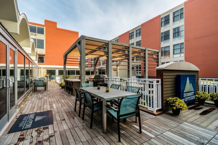 A modern rooftop patio with outdoor seating and a pergola, set against an urban backdrop.