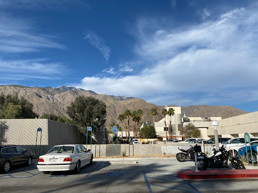 A serene view of mountains under a partly cloudy sky, featuring vehicles parked in a lot and palm trees in the foreground.