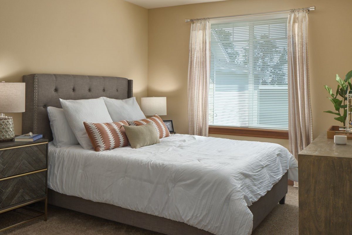 A cozy bedroom with a neatly made bed, decorative pillows, and natural light streaming through the window.