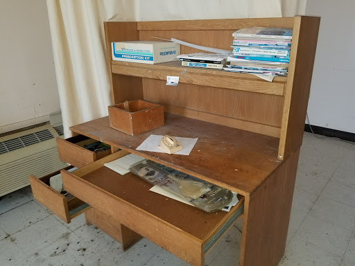 A wooden desk with an upper shelf, cluttered with papers and office supplies.