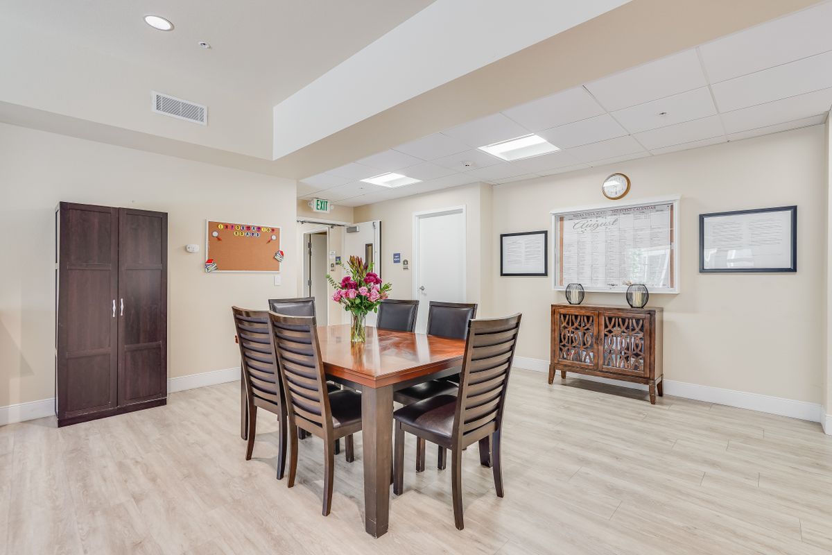 A modern dining room with a wooden table and six chairs, adorned with a floral centerpiece.