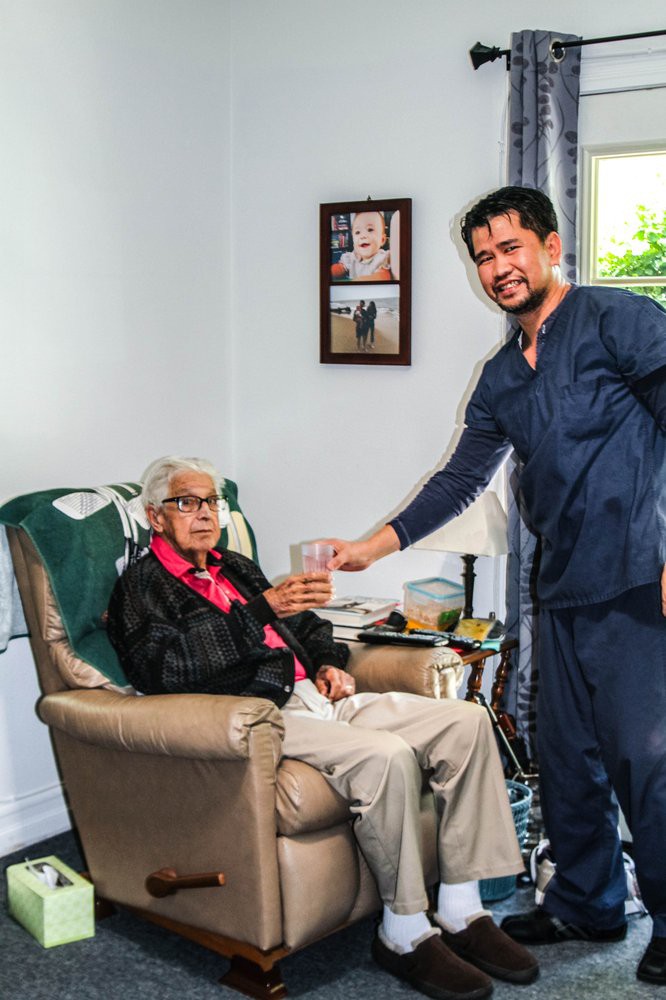 A caregiver assisting an elderly person in a living room setting.