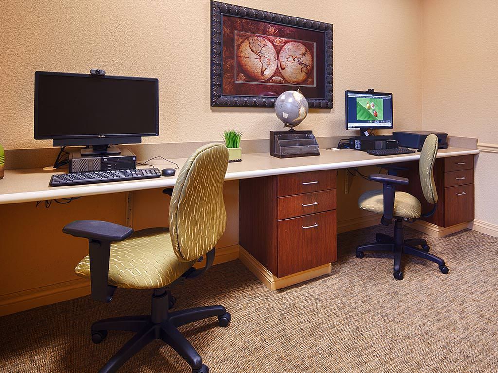 A neatly organized office space with two computers set up on a long desk, accompanied by comfortable chairs and decorated with wall art.