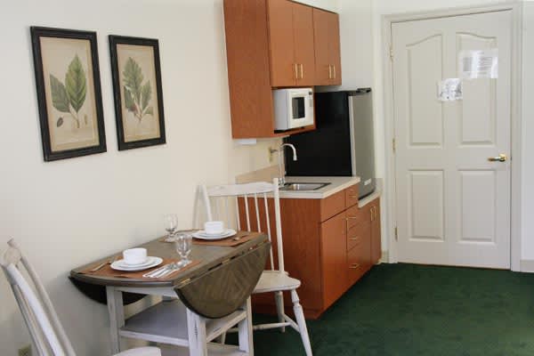 A compact kitchen and dining area featuring a small table with chairs, cabinetry, sink, microwave, and framed artwork on the wall.