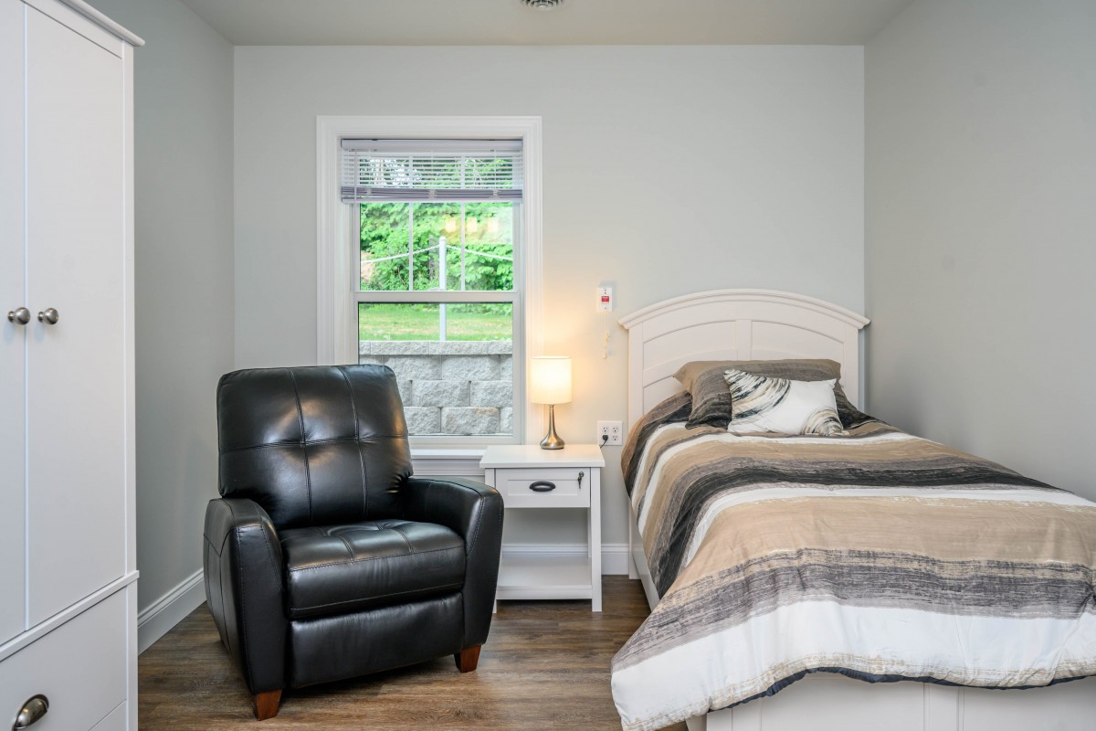 Cozy bedroom with a recliner, bed, and nightstand under a window.