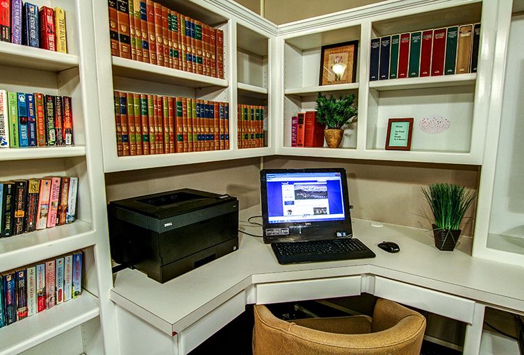 A well-organized home office with a computer, printer, and bookshelf filled with books.