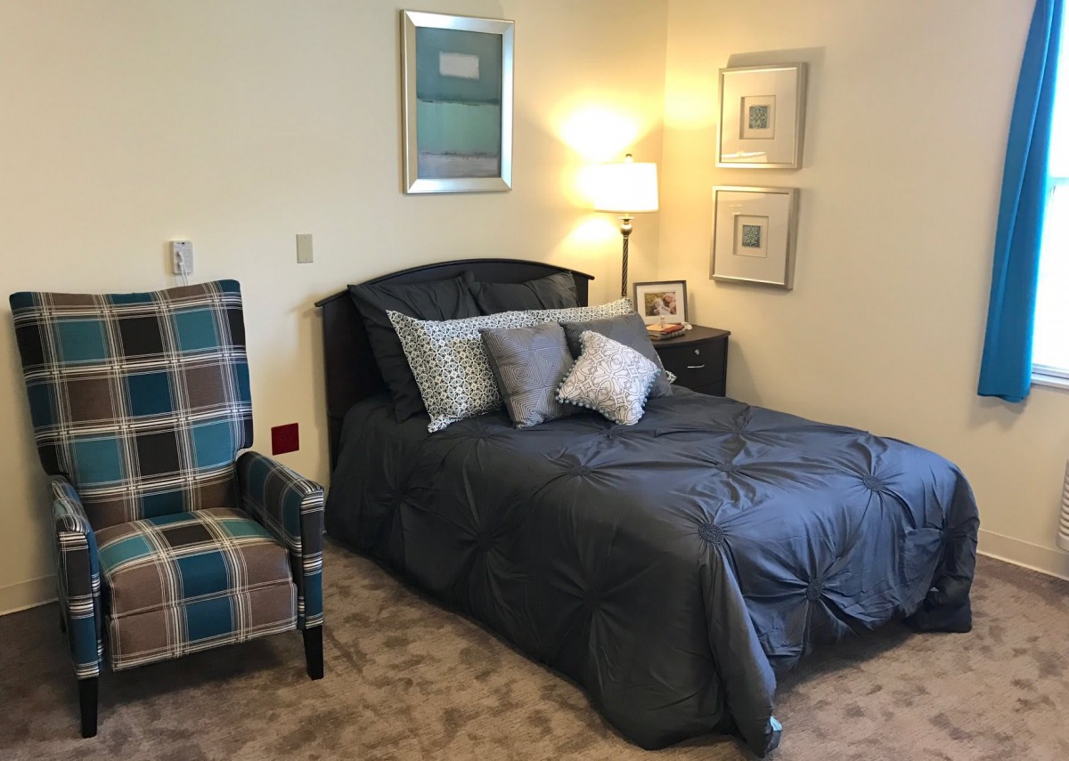 A cozy bedroom with a neatly made bed, stylish chair, and soft lighting.