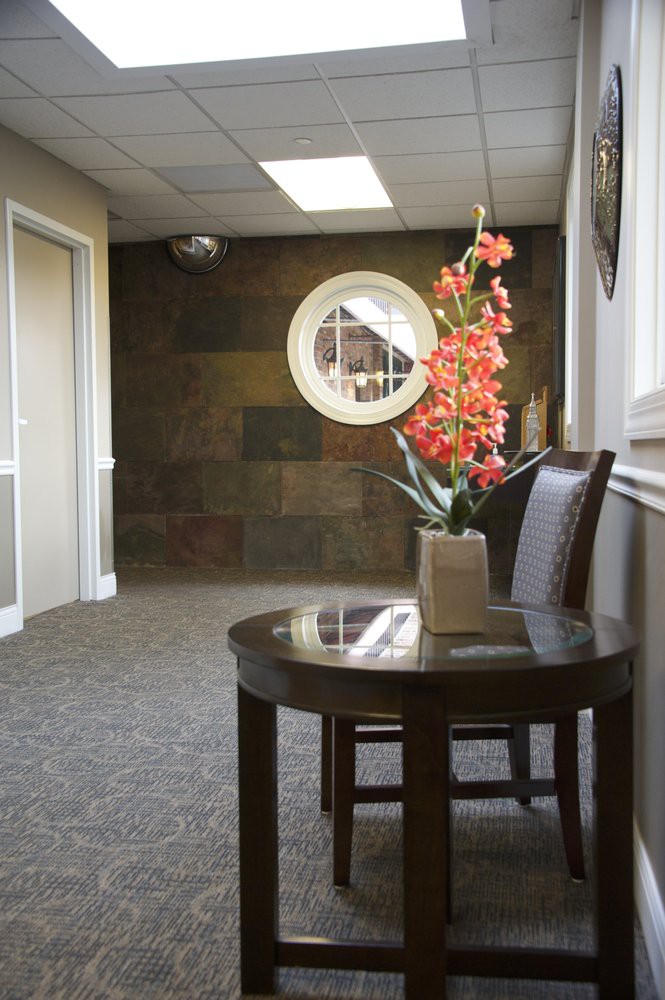 A waiting room with a round window, decorated with flowers on a table and chairs.