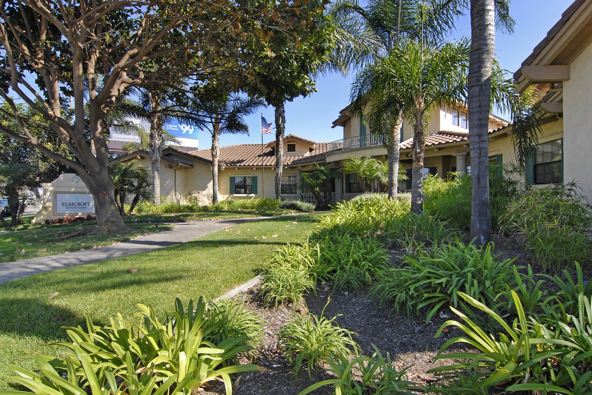 A beautiful residential home surrounded by lush gardens and palm trees on a sunny day.