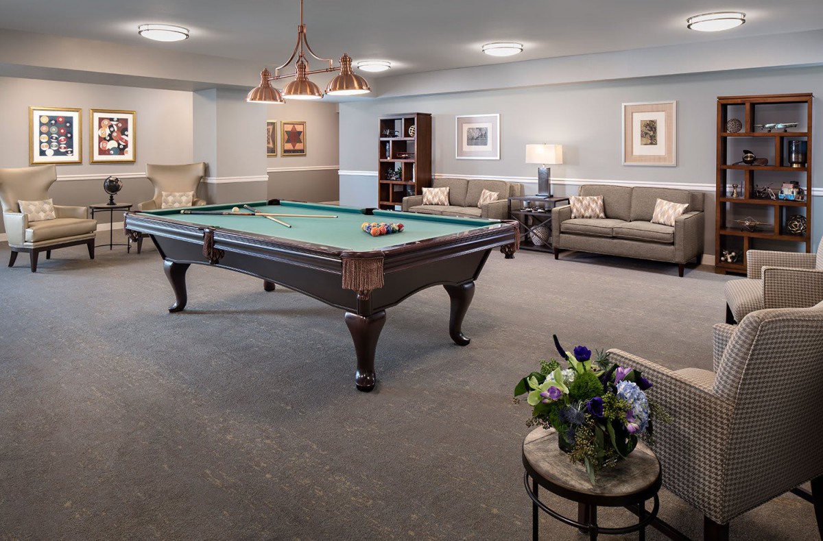 A cozy billiard room featuring a central pool table, comfortable sofas, elegant lighting, and tasteful decor.