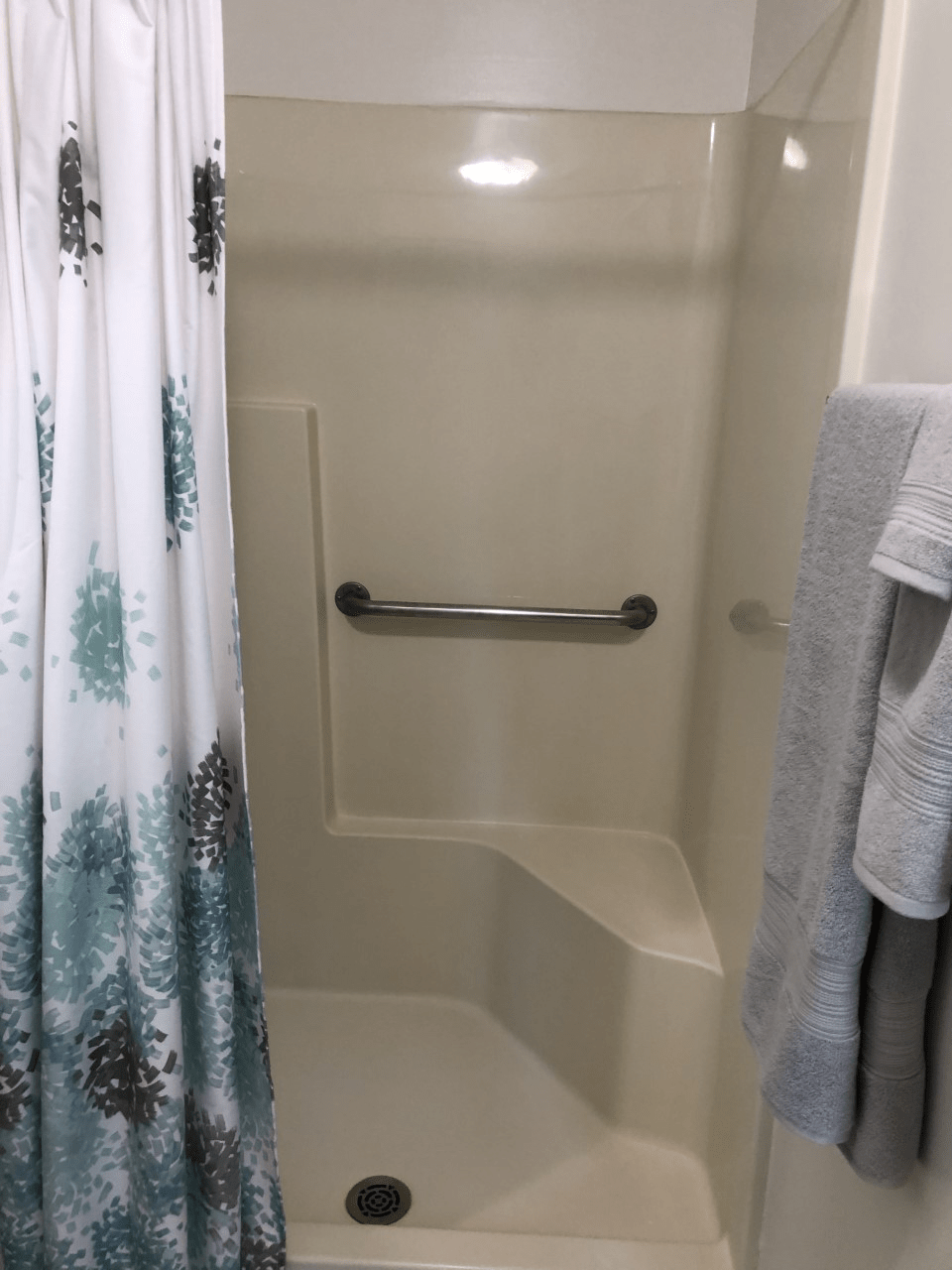 A bathroom with a shower equipped with a grab bar and patterned shower curtain.