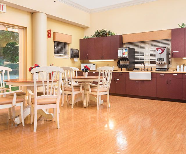 A cozy dining area with several tables and chairs, featuring a wooden floor and a counter with a coffee machine.