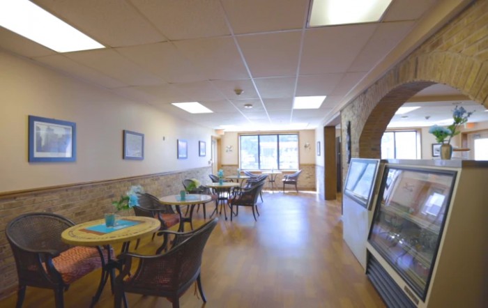 A cozy cafe with tables and chairs arranged near large windows, allowing natural light to brighten the space.