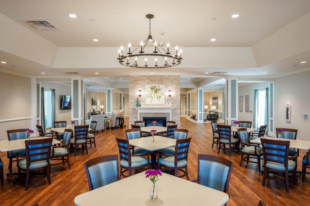 An elegantly designed dining room featuring a large chandelier, a central fireplace, and neatly arranged tables and chairs.