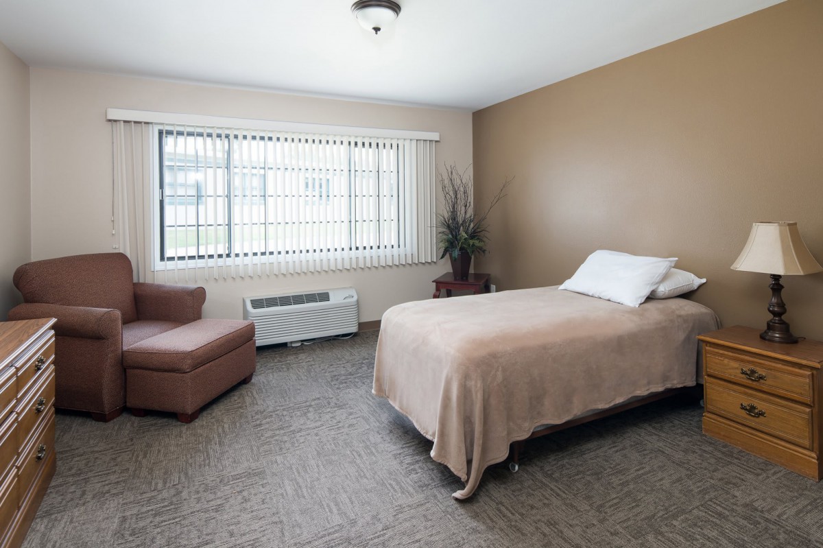 A minimalist bedroom with a single bed, beige decor, and large windows.