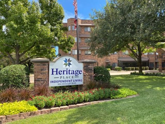 A sign for Heritage Place Independent Living in front of a building surrounded by trees and a well-maintained lawn.