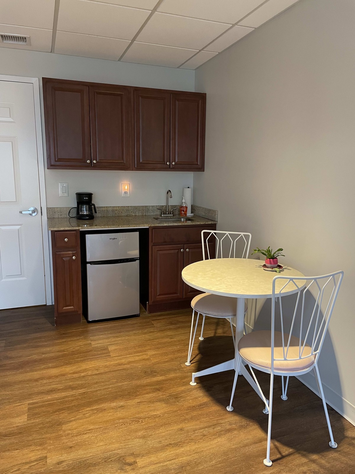 A compact kitchenette with a small fridge, coffee maker, and dining area.