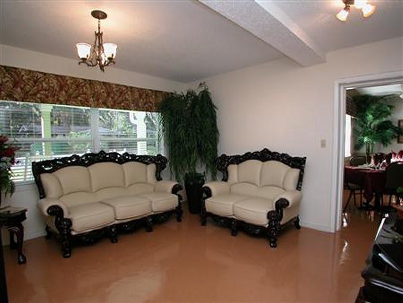 A cozy living room with elegant sofas and a chandelier, featuring large windows and a decorative plant.