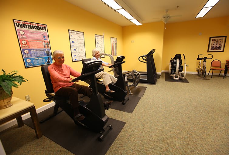 Senior citizens exercising on recumbent bikes in a gym with yellow walls.