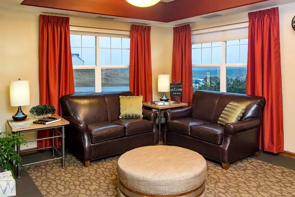 A cozy living room with leather sofas and bright red curtains overlooking a scenic view.