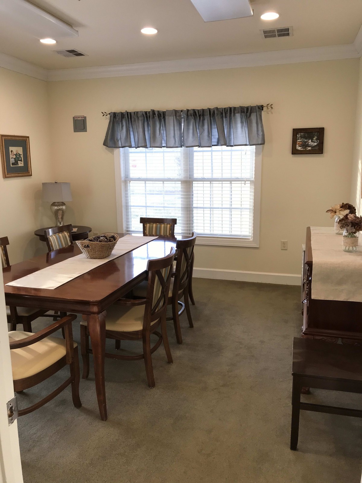 A cozy dining room with a wooden table and chairs, featuring a large window with blue curtains.