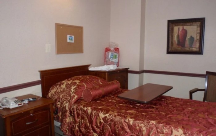 A cozy bedroom with a red patterned comforter and wooden furniture.