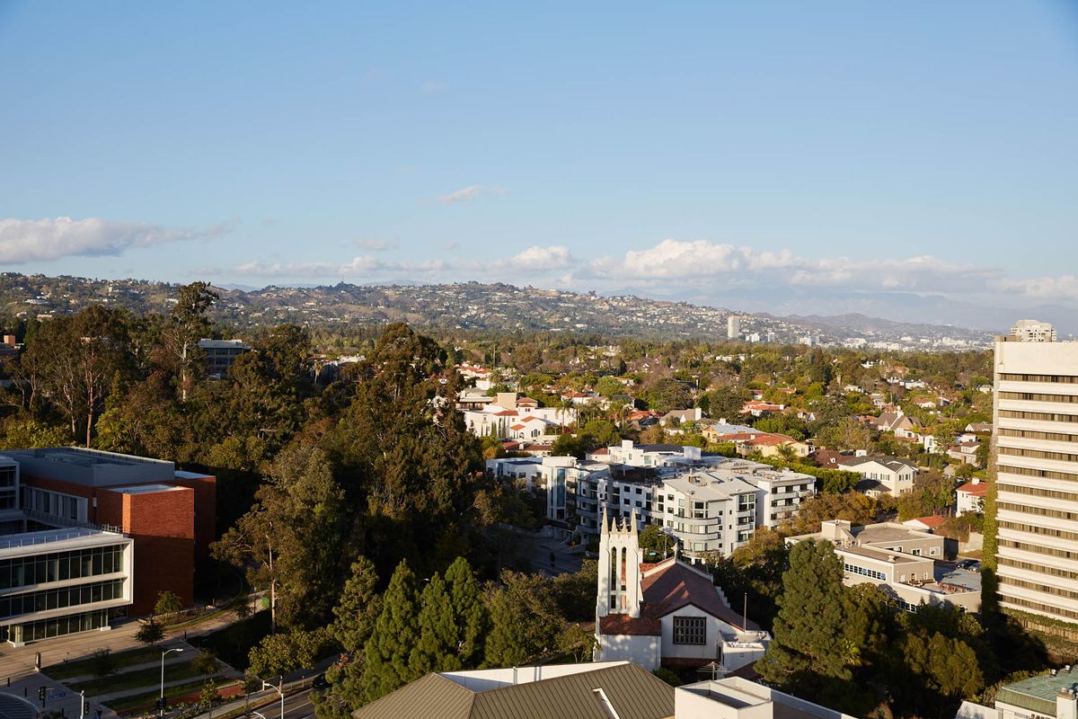 A scenic view of an urban landscape with distant mountains, featuring buildings and lush greenery under a clear blue sky.