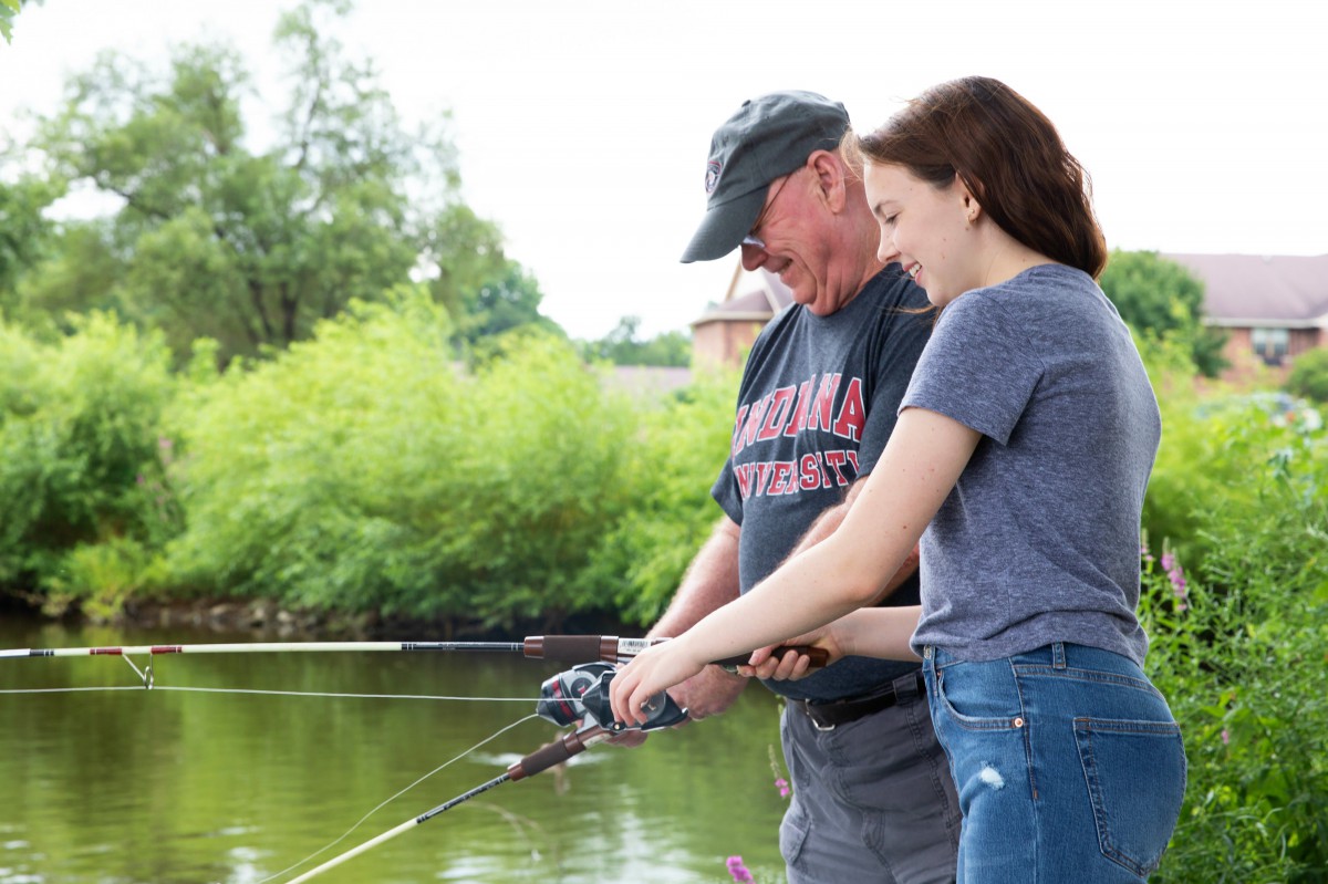 A young woman and an older man enjoying a day of fishing together by the lake.