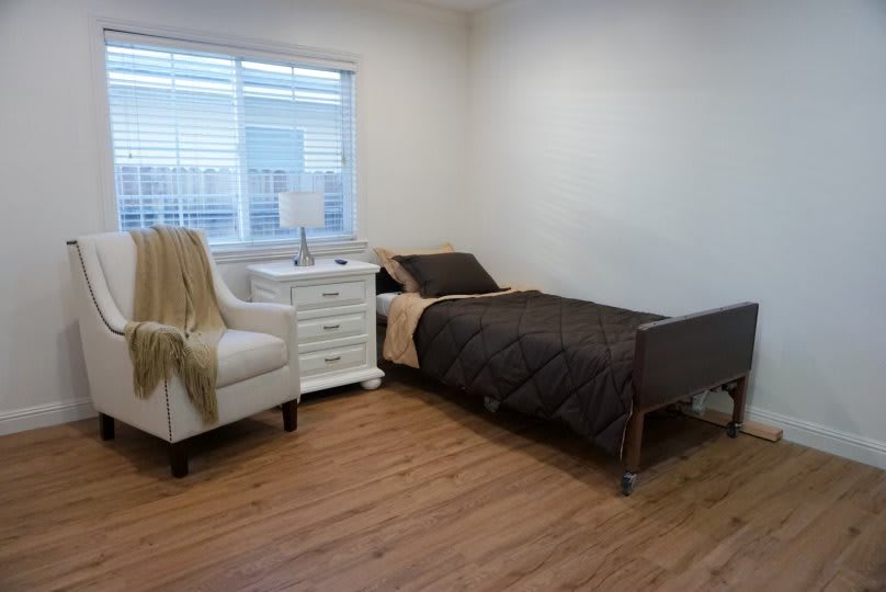 A minimalist bedroom with a single bed, armchair, and nightstand by the window.
