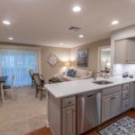 A modern open floor plan featuring a kitchen with white countertops, adjacent to a cozy living room and dining area, all well-lit by recessed lighting.